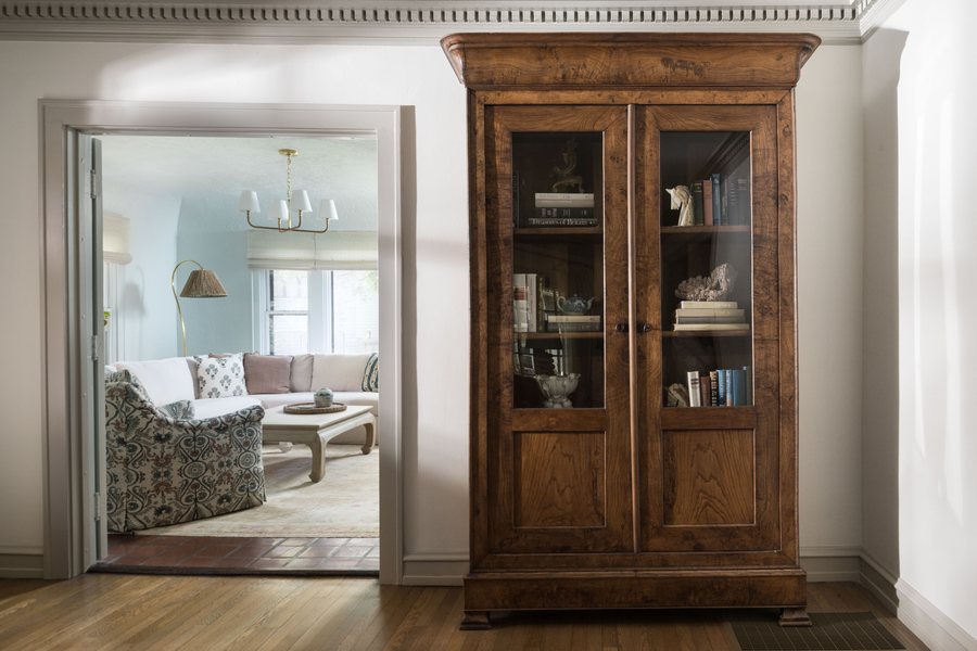 Antique burl wood cabinet framing a view into a soft blue sunroom, designed by Kimberly Knight of Twig and Trove Interiors